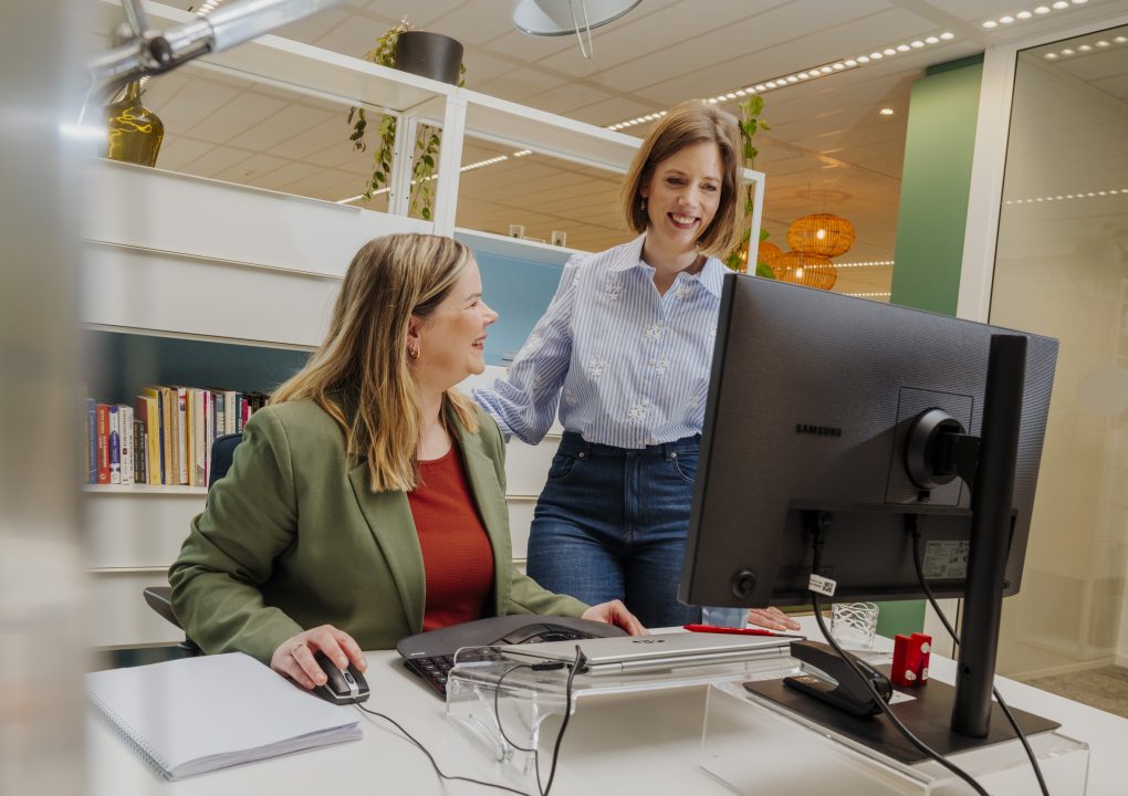 Natascha (links) zit achter computer, Joyce staat rechts van Natascha en lacht naar het scherm